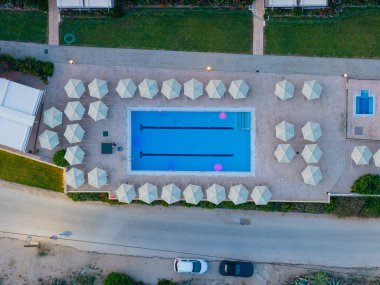 Etrafı şemsiye desenleriyle çevrili bir tatil köyü yüzme havuzunun minimalist yukarıdan aşağıya manzarası. Sakin, lüks bir oteli ve tatili temsil eden geometrik bir yaz geçmişi..