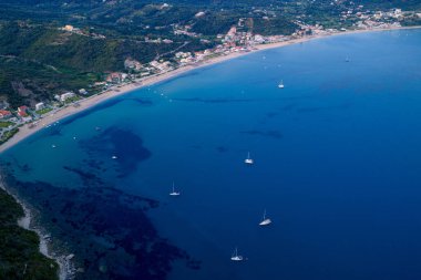 Korfu, Agios Georgios Pagon 'un geniş körfezi üzerinde yüksek irtifa drone görüntüsü. Yelkenliler, Yunan adası tatil beldesinin engin, kumlu kıyı şeridi boyunca derin mavi İyon Denizi 'ni noktalıyor..