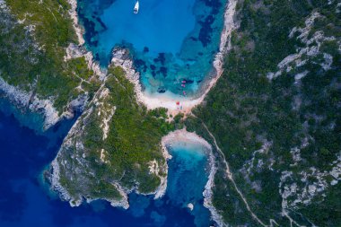 Top-down aerial drone view of the famous Porto Timoni twin beach on Corfu island, Greece. A narrow isthmus separates two coves with crystal-clear turquoise water, showcasing a unique natural wonder.