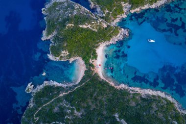 Yunanistan 'ın Corfu kentindeki eşsiz Porto Timoni çifte plajının baş aşağı havadan çekilmiş fotografı, canlı mavi ve turkuaz sulardaki berrak deniz yatağını ve yakınındaki bir yatı gösteriyor..