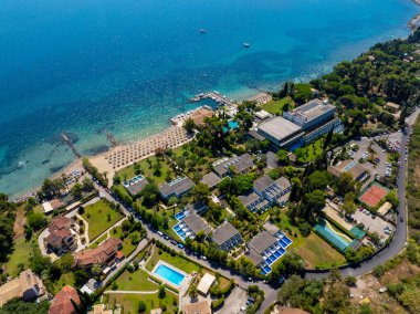 Yunanistan 'ın Korfu kentinde lüks bir sahil beldesinin insansız hava aracı görüntüsü. Turkuaz suyu, özel havuzları ve mükemmel bir yaz tatili ve seyahat yeri için kumlu plajı olan güzel bir sahil şeridi.