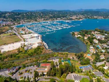 Expansive aerial panorama of Gouvia Marina in Corfu, Greece, a major yachting destination in the Ionian Sea. A luxury coastal resort is visible in the foreground on a sunny day