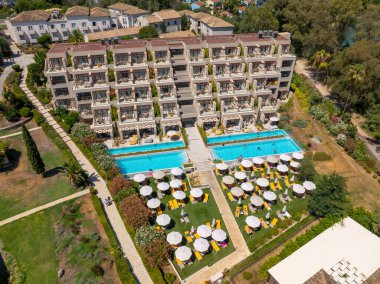 Modern hotel architecture at a luxury resort in Corfu, Greece, seen from an aerial perspective. View of the building's balconies and two swimming pools with sun loungers on a green lawn
