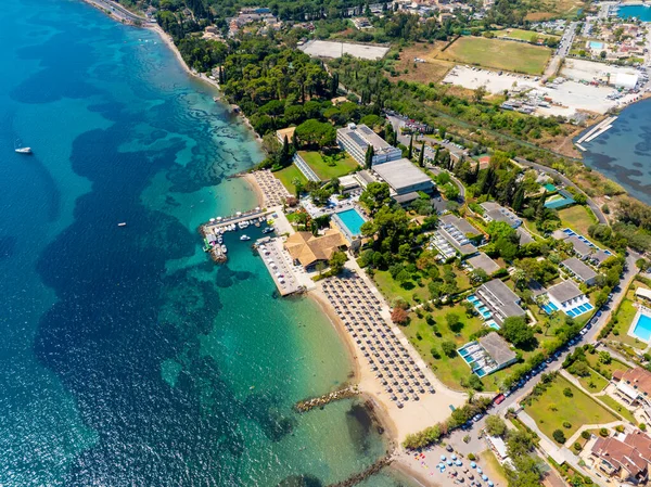 Aerial panorama of a stunning beach resort on Corfu island, Greece. Drone view of the hotel, pools, and clear Ionian Sea, with the lush green coastline stretching into the distance