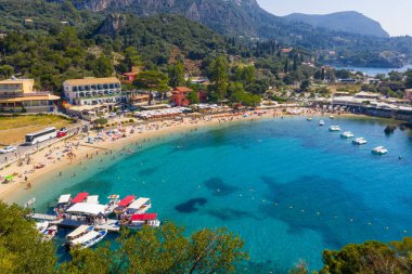Breathtaking aerial panoramic view of a beautiful Mediterranean bay in Greece. A picturesque coastal village and a sunny beach with tour boats docked on the crystal clear turquoise sea