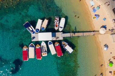 Top-down aerial drone view of tour boats moored at a floating pier in a crystal clear turquoise sea. A unique abstract perspective of summer travel and transportation in Greece