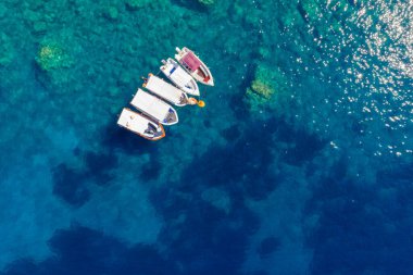 Minimalist top-down aerial shot of four small boats floating on the deep blue, transparent sea with sunlight sparkling on the water's surface. A serene and beautiful abstract marine background