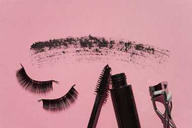 Black false lashes strips, mascara, curler on pink background  clipart