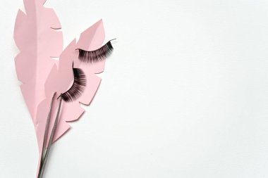 Black false lashes strips with tweezers on pink paper leaves  clipart