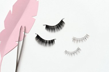 Black false lashes strips and tweezers on white background  clipart