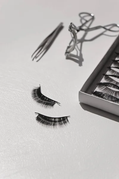 Black false lashes strips set with curler and tweezers on white