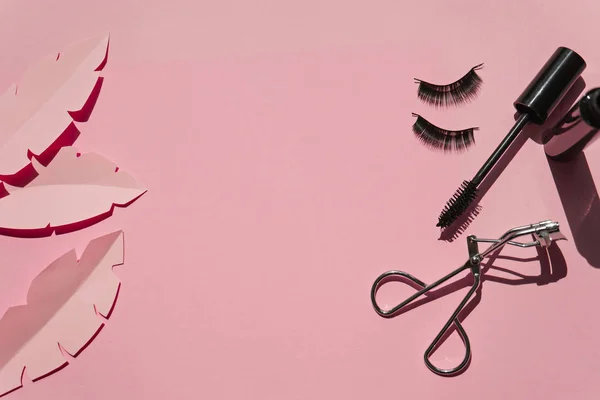 Black false lashes strips,mascara, curler on pink background