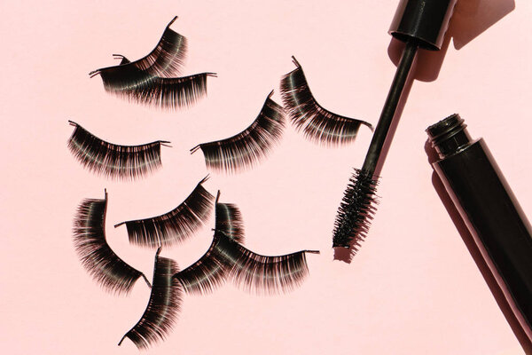 Black false lashes strips with mascara on pink background 