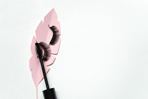 Black false lashes strips  wiht mascara on pink paper leaves 