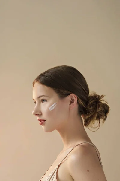 portrait of young beautiful woman with cream on her face on beige background