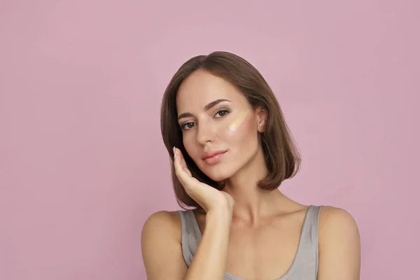 Young woman with cosmetic foundation on skin on pink background