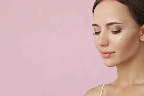 Young woman with cosmetic foundation on skin on pink background