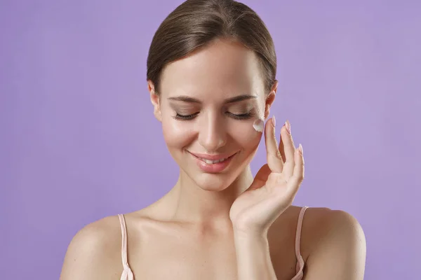 Porträt Einer Frau Die Kosmetische Creme Auf Violettem Hintergrund Aufträgt — Stockfoto