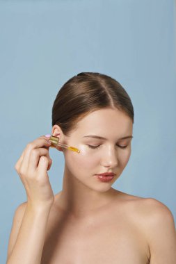 portrait of young woman applying serum on her face on blue background  clipart