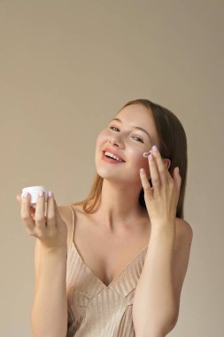 kozmetik krem bej arka yüzünde uygulayarak genç gülümseyen kadın portresi 