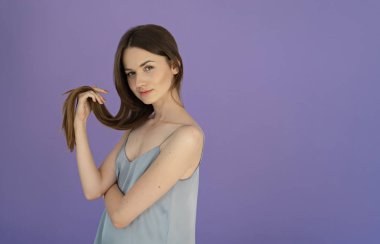 uzun parlak saçlar tutarak ve kameraya mor arka plan üzerinde seyir genç kadın portresi