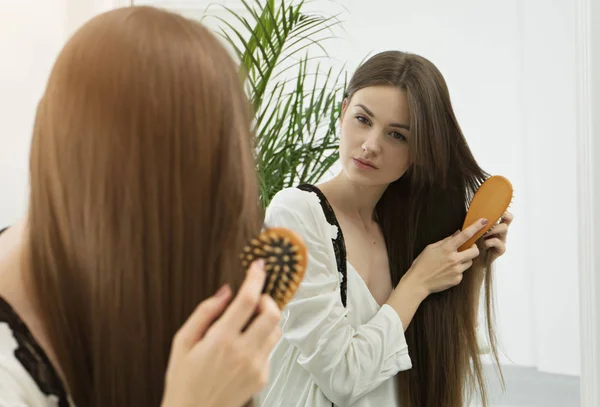 若い女性が長い髪をとかすのミラーで反射 — ストック写真