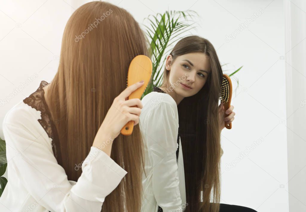 Reflection in mirror of young woman combing long hair 