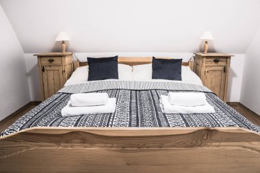 Rustik ahşap yatak, Çift Kişilik Yatak, başucu masaları, yorgan ve havlu ile rahat kırsal otel odasında