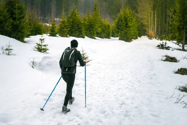 Young sports woman with backpack walking through snowy mountains, Sport in winter background, Nordic walking in snowy nature