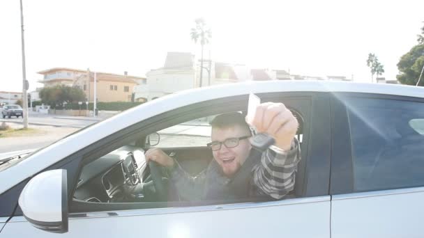 Joven hombre caucásico feliz sentado en el coche con las llaves del coche — Vídeo de stock