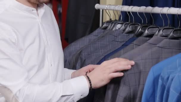 Мужчина выбирает деловой костюм в магазине мужской одежды — стоковое видео