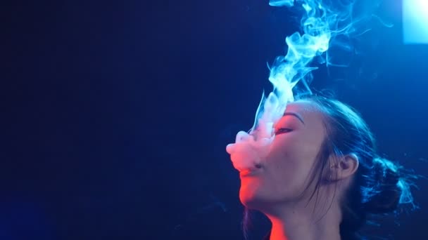Jovem fuma cigarro eletrônico em luz colorida. Vida noturna e conceito de vape — Vídeo de Stock