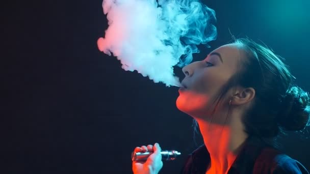 Mujer joven fuma cigarrillo electrónico en luz de color. Vida nocturna y concepto de vapor — Vídeo de stock