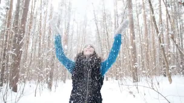 Młoda kobieta rzuca śnieg się z ładnym uśmiechem w lesie zimą — Wideo stockowe