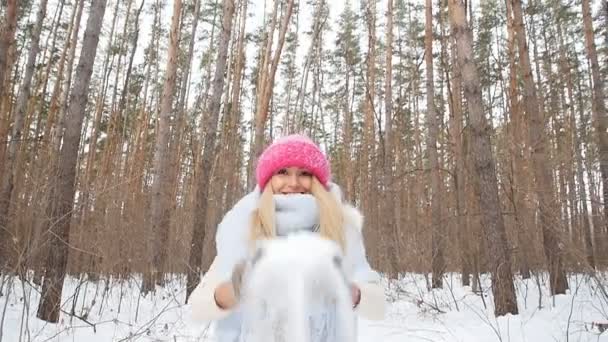 Mujer joven arroja nieve con una bonita sonrisa en el bosque de invierno — Vídeo de stock