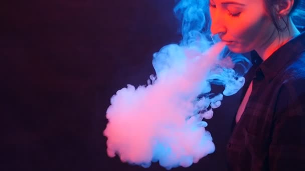 Une jeune femme fume une cigarette électronique. Fumer dans la lumière de couleur — Video