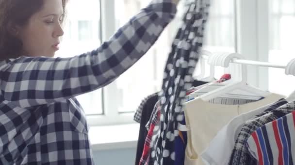 Een jonge vrouw kiest kleding in een winkel — Stockvideo