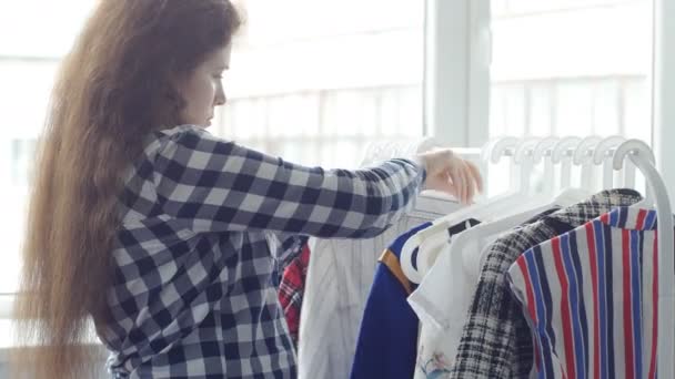 Een jonge vrouw kiest kleding in een winkel — Stockvideo