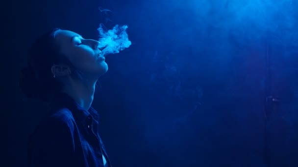 Jeune femme dans des lumières vives avec de la fumée colorée. Fumer des cigarettes électroniques concept — Video
