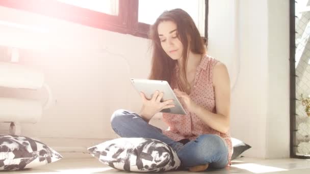 Jovem mulher em um quarto ensolarado usando um tablet — Vídeo de Stock