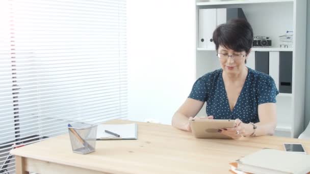 Orta yaşlı bir kadın ofiste tablet kullanma — Stok video