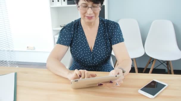 Una mujer de mediana edad en la oficina usando una tableta — Vídeo de stock