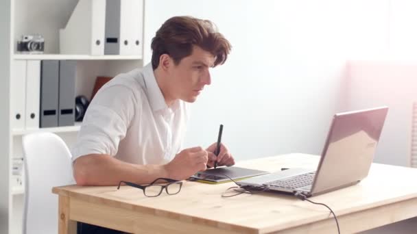 Περιστασιακό αρσενικό σχεδιαστής χρήση tablet γραφικών σε ένα φωτεινό γραφείο — Αρχείο Βίντεο