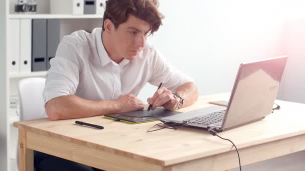Περιστασιακό αρσενικό σχεδιαστής χρήση tablet γραφικών σε ένα φωτεινό γραφείο — Αρχείο Βίντεο
