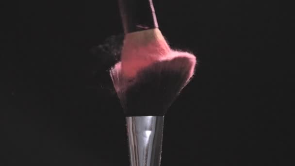 Pincéis de maquiagem com pó rosa sobre fundo preto em câmera lenta — Vídeo de Stock