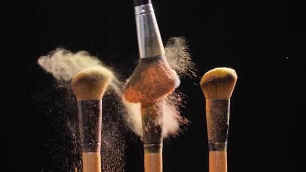 Cosmetische penselen met gouden cosmetische poeder op zwarte achtergrond — Stockvideo