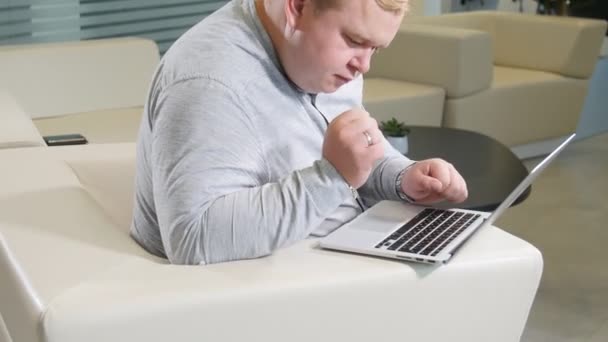 Концепция работы офиса. Мужчина смотрит на свой ноутбук, сидит в офисе на уютном белом диване — стоковое видео