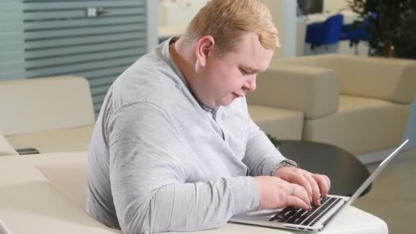 Concepto de trabajo de oficina. El hombre está navegando en su computadora portátil, sentado en la oficina en el acogedor sofá blanco — Vídeos de Stock