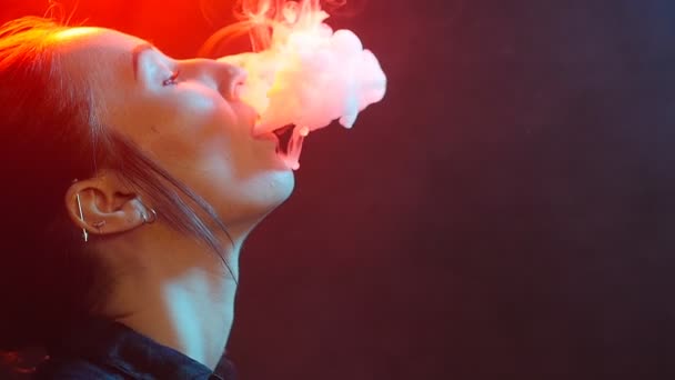 Nacht leven concept. Jonge vrouw rookt elektronische sigaret in de kleur licht — Stockvideo