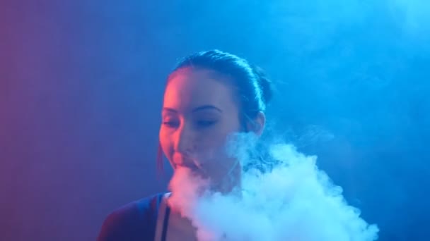 Концепція нічного життя. Молода жінка курить електронну сигарету в кольоровому світлі — стокове відео